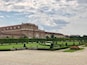 A large historic building with a symmetrical facade, surrounded by well-manicured gardens and hedges.