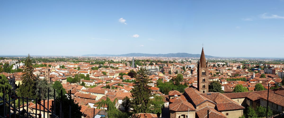 A cityscape with a prominent church tower, surrounded by red-roofed buildings and greenery.