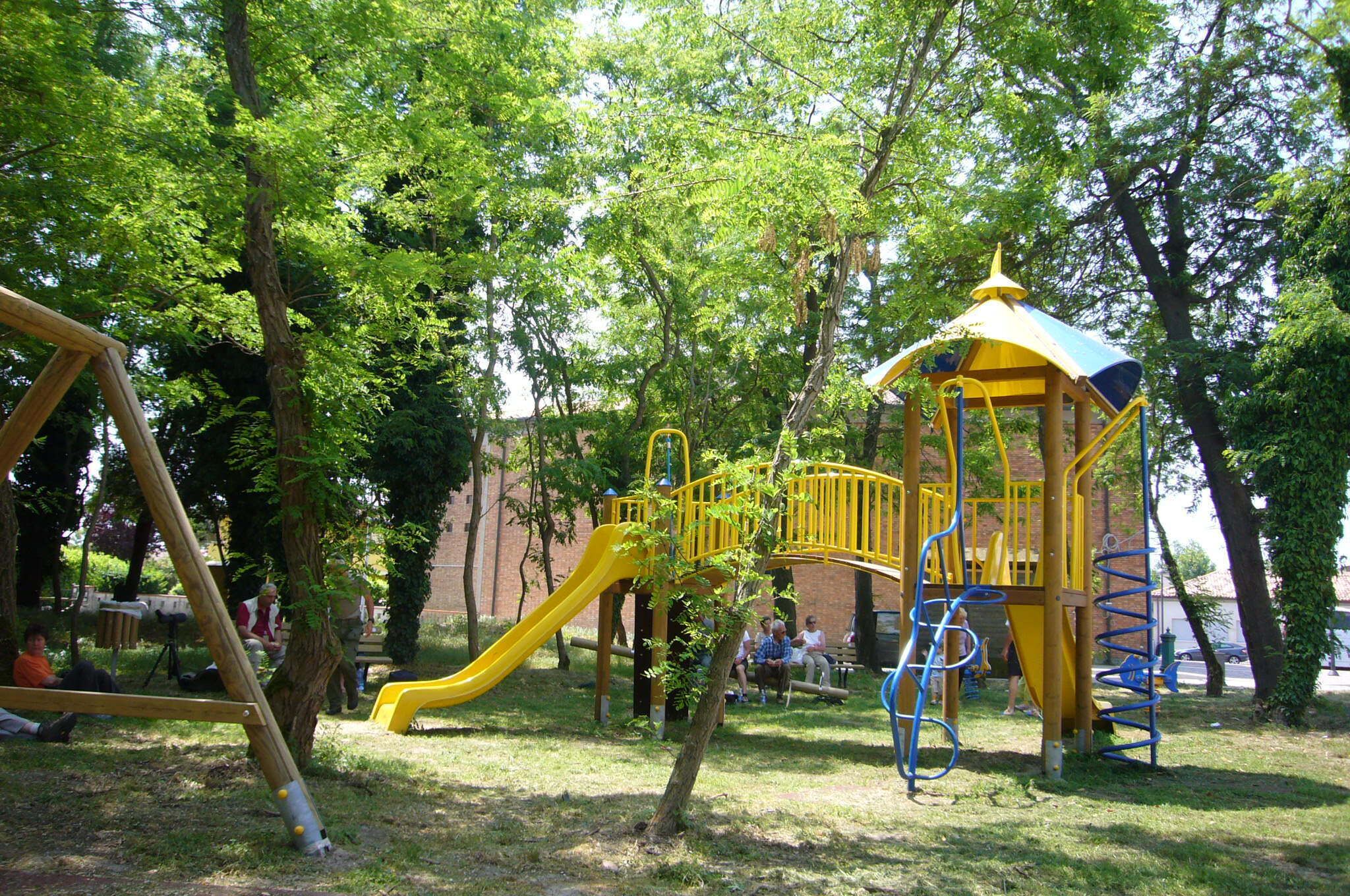 A playground with a yellow slide, a swing set, and a covered playhouse.