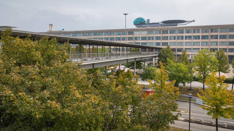 A modern building with a glass facade and a pedestrian bridge.