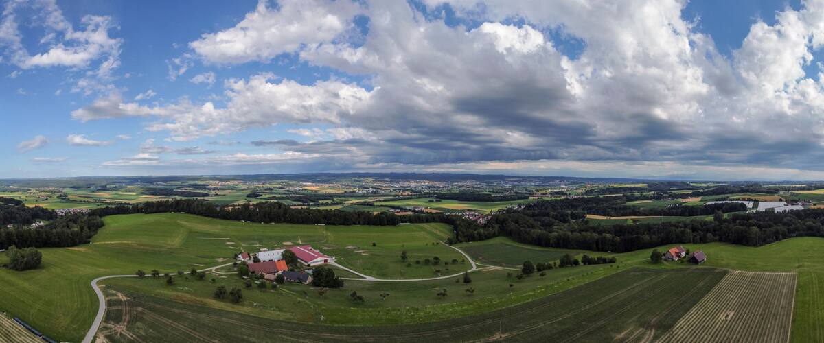 A rural landscape with rolling fields, a few scattered houses, and a large body of water in the distance.