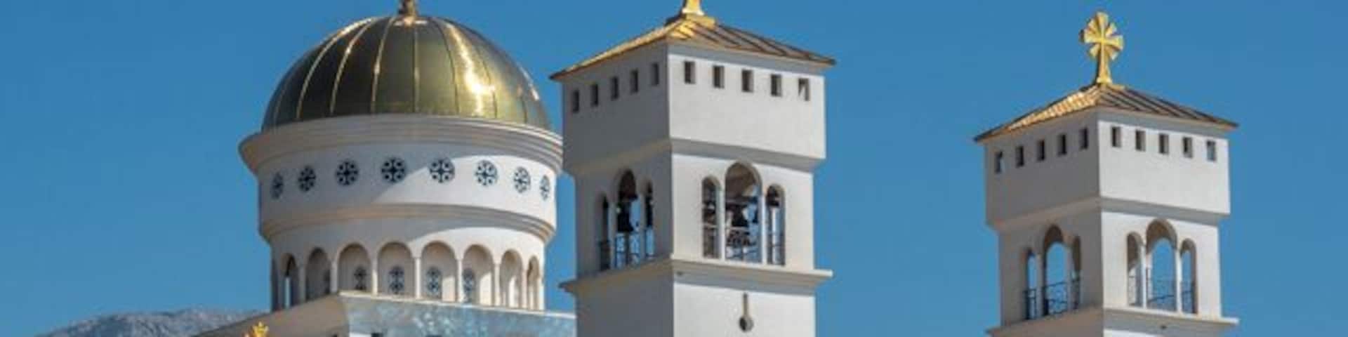 A white church with golden domes and towers, surrounded by trees and mountains.