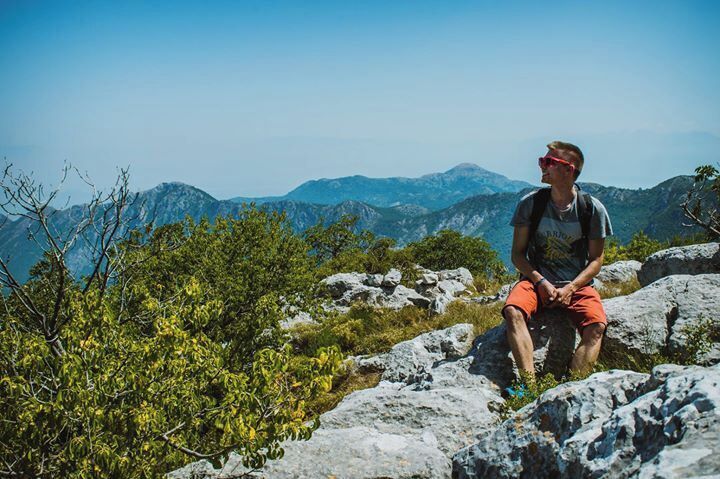 A person sitting on a rocky outcrop with mountains in the background.