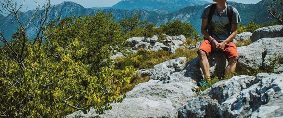 A person sitting on a rocky outcrop with mountains in the background.