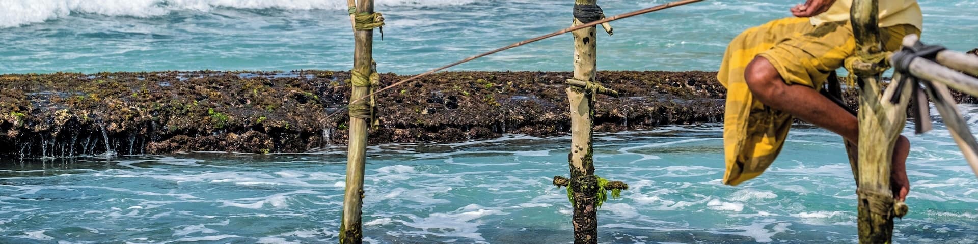 Ritipanna is the Sinhalese term for stilt fishing, which is a traditional method for fishing practiced by most fishermen along the southern coast of Sri Lanka. This art is popularly seen in areas such as Ahangama, Koggala, Welipenna, Kathaluwa and Thalarambe. A narrow pole is tied to a stick that is anchored on the sea bed. Fisher folk climb onto this stick and settle on the pole for a few hours in an effort to catch some fish.
Fishermen found on stilts are those who do not have access to sophisticated equipment for fishing. These men can make a living simply with the help of two wooden poles to make a stilt. One pole is nailed onto the sea bed and the other is placed like a cross bar and acts as a plank for the fishermen to sit on. Each stilt can accommodate only one fisherman. For catching fish, they create a rod made of Kithul, and a small plastic bag is tied around their waist to hold the fish that they catch. With one hand they hold onto the stilt and with the other they hold the rod that catches fish. The tradition of stilt fishing will always be practiced by those who cannot afford to invest in modern fishing equipment.