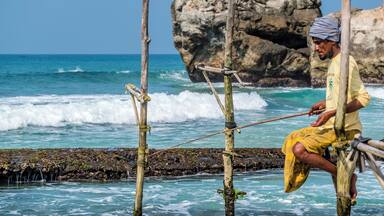 Ritipanna is the Sinhalese term for stilt fishing, which is a traditional method for fishing practiced by most fishermen along the southern coast of Sri Lanka. This art is popularly seen in areas such as Ahangama, Koggala, Welipenna, Kathaluwa and Thalarambe. A narrow pole is tied to a stick that is anchored on the sea bed. Fisher folk climb onto this stick and settle on the pole for a few hours in an effort to catch some fish.
Fishermen found on stilts are those who do not have access to sophisticated equipment for fishing. These men can make a living simply with the help of two wooden poles to make a stilt. One pole is nailed onto the sea bed and the other is placed like a cross bar and acts as a plank for the fishermen to sit on. Each stilt can accommodate only one fisherman. For catching fish, they create a rod made of Kithul, and a small plastic bag is tied around their waist to hold the fish that they catch. With one hand they hold onto the stilt and with the other they hold the rod that catches fish. The tradition of stilt fishing will always be practiced by those who cannot afford to invest in modern fishing equipment.
