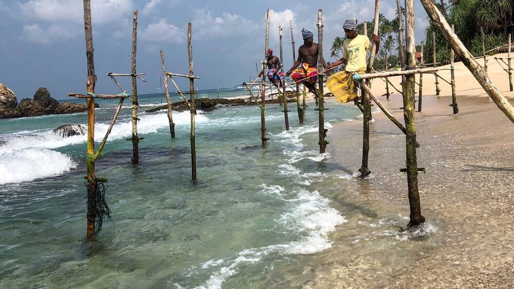 A beach with wooden structures in the water and people standing on them.