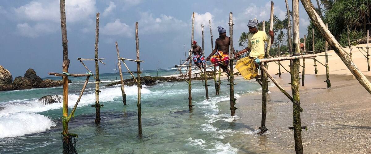 A beach with wooden structures in the water and people standing on them.