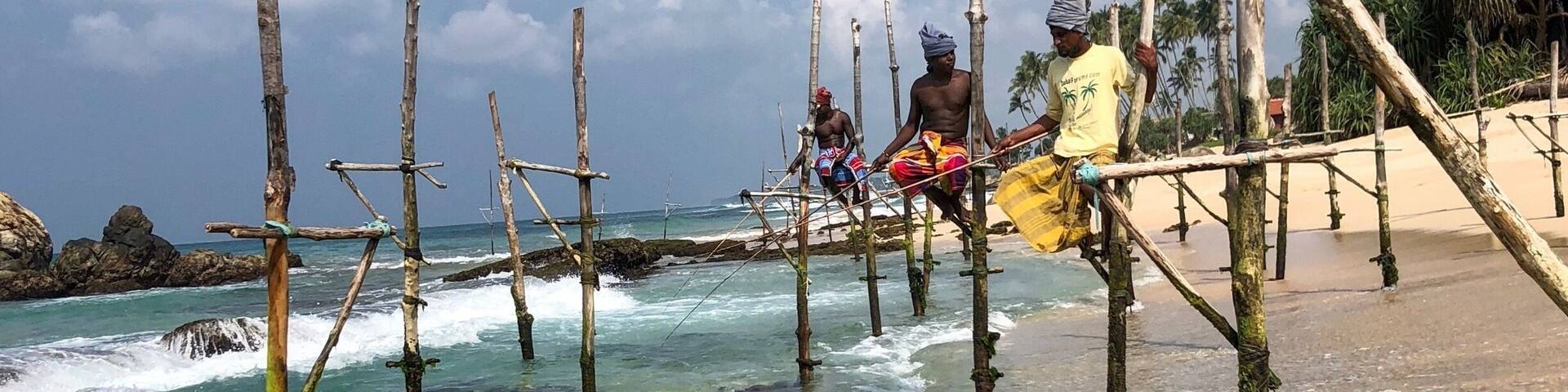 A beach with wooden structures in the water and people standing on them.