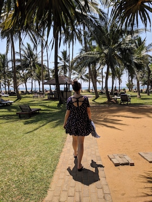 Uma mulher caminhando por um caminho pavimentado, cercada por palmeiras e cadeiras de praia.