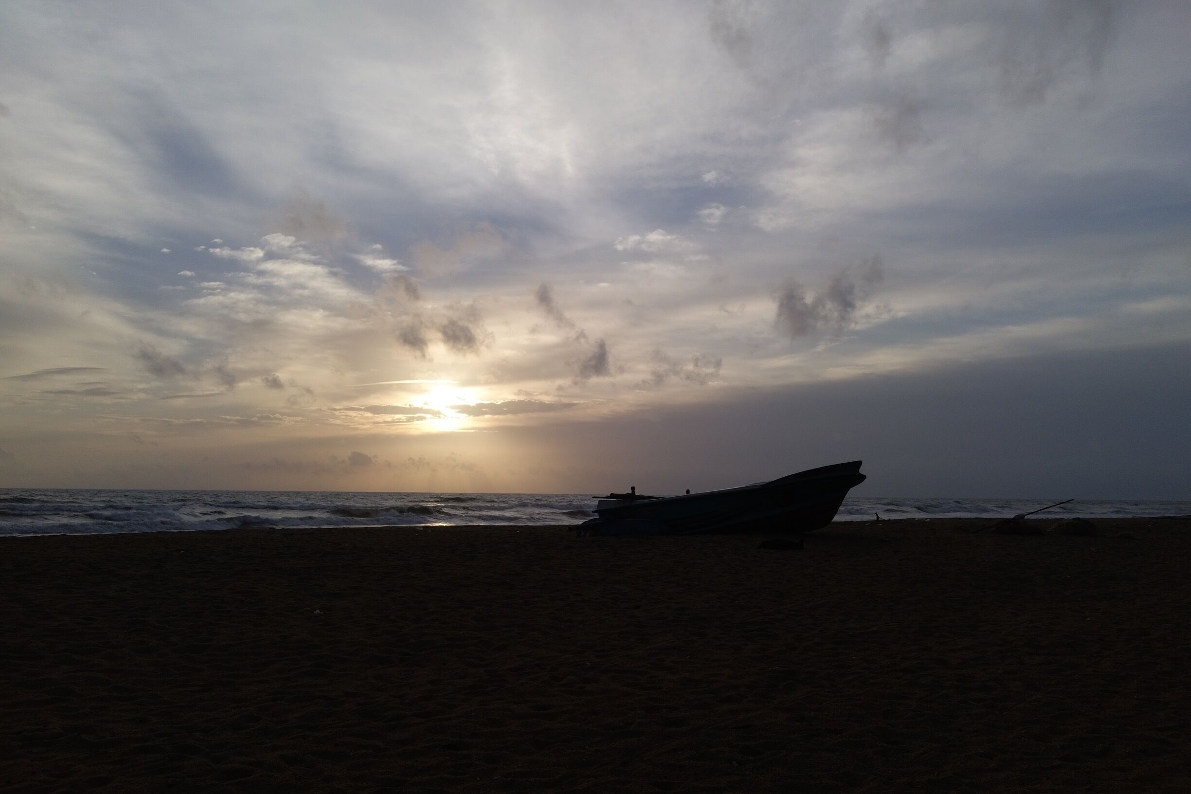 A beach with a boat and waves under a cloudy sky.