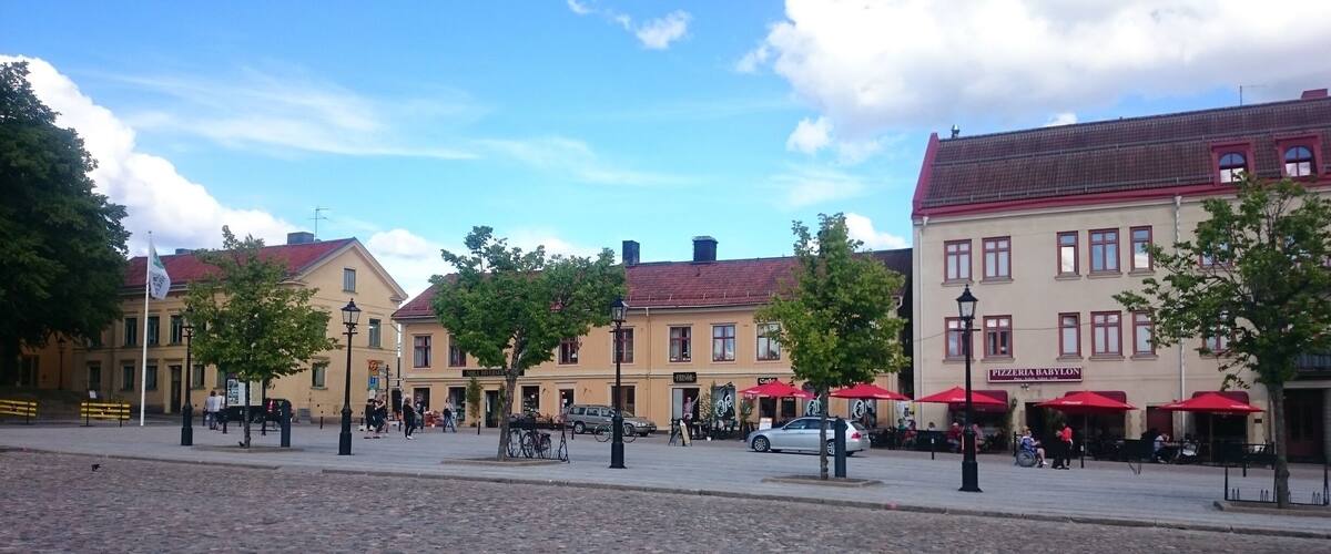 A cobblestone square with historic buildings, outdoor cafes, and a flagpole.