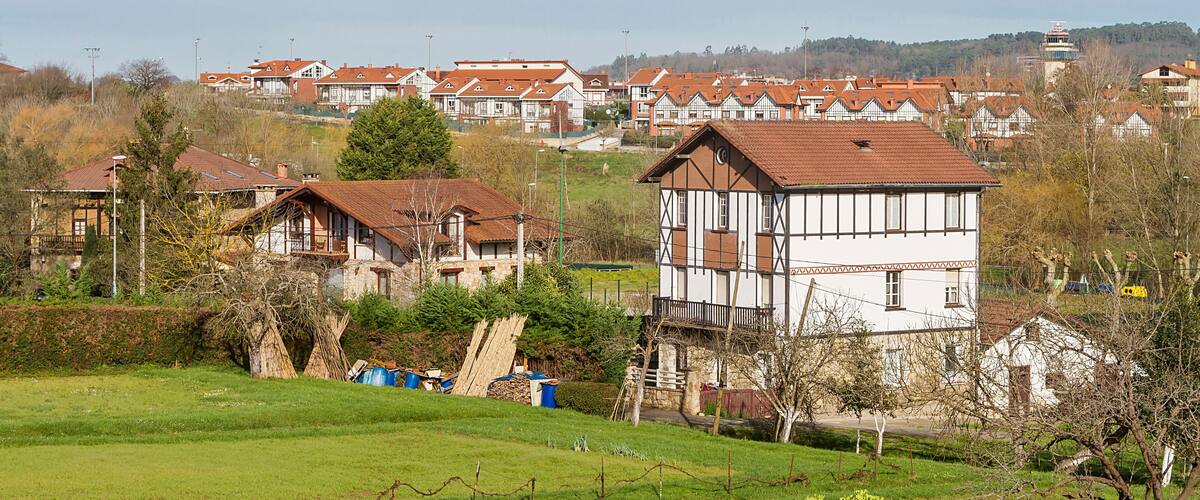 A rural village with traditional half-timbered houses, a green field, and a hill in the background.