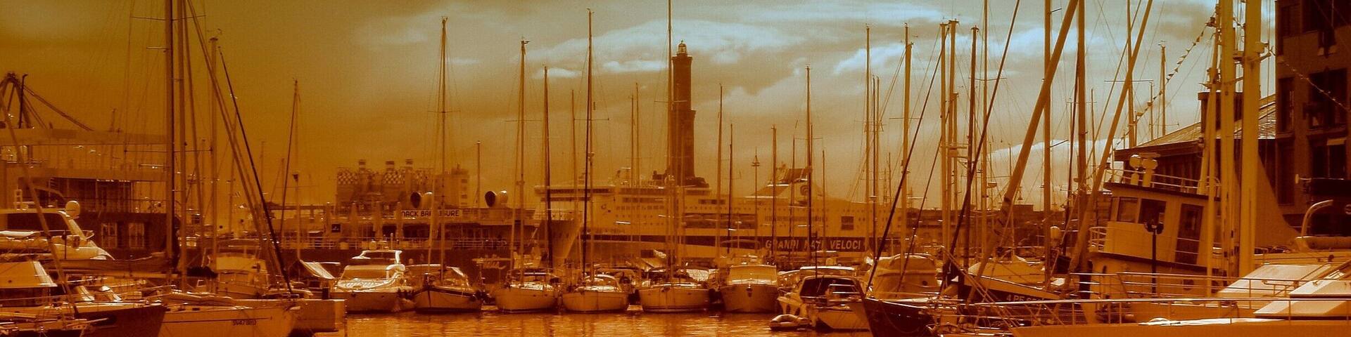 A harbor with numerous sailboats docked, a prominent lighthouse in the background, and a cityscape with buildings.