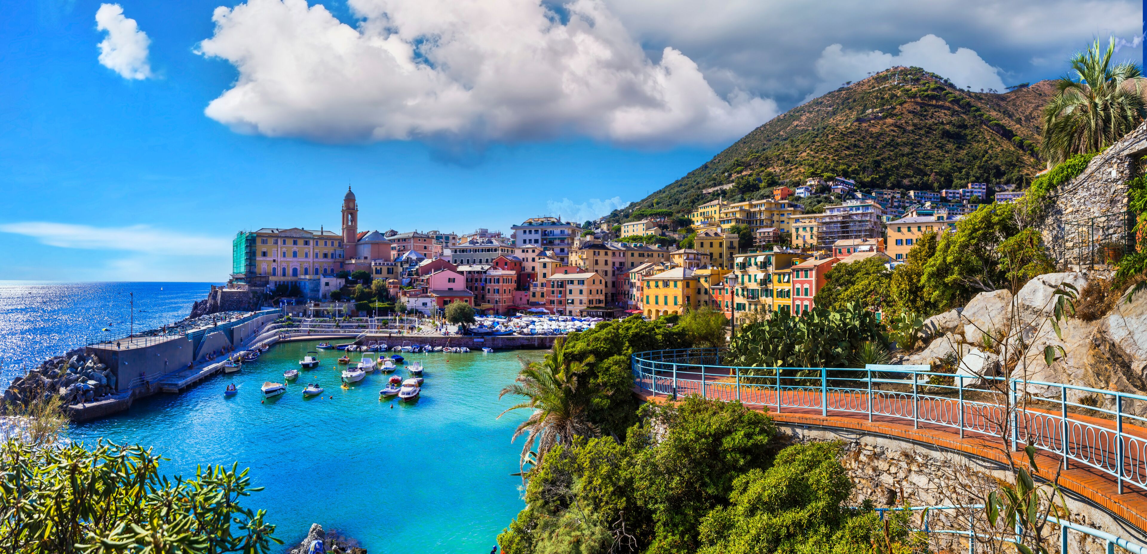 Un pueblo costero con edificios de colores, una torre destacada y barcos amarrados a lo largo del muelle.