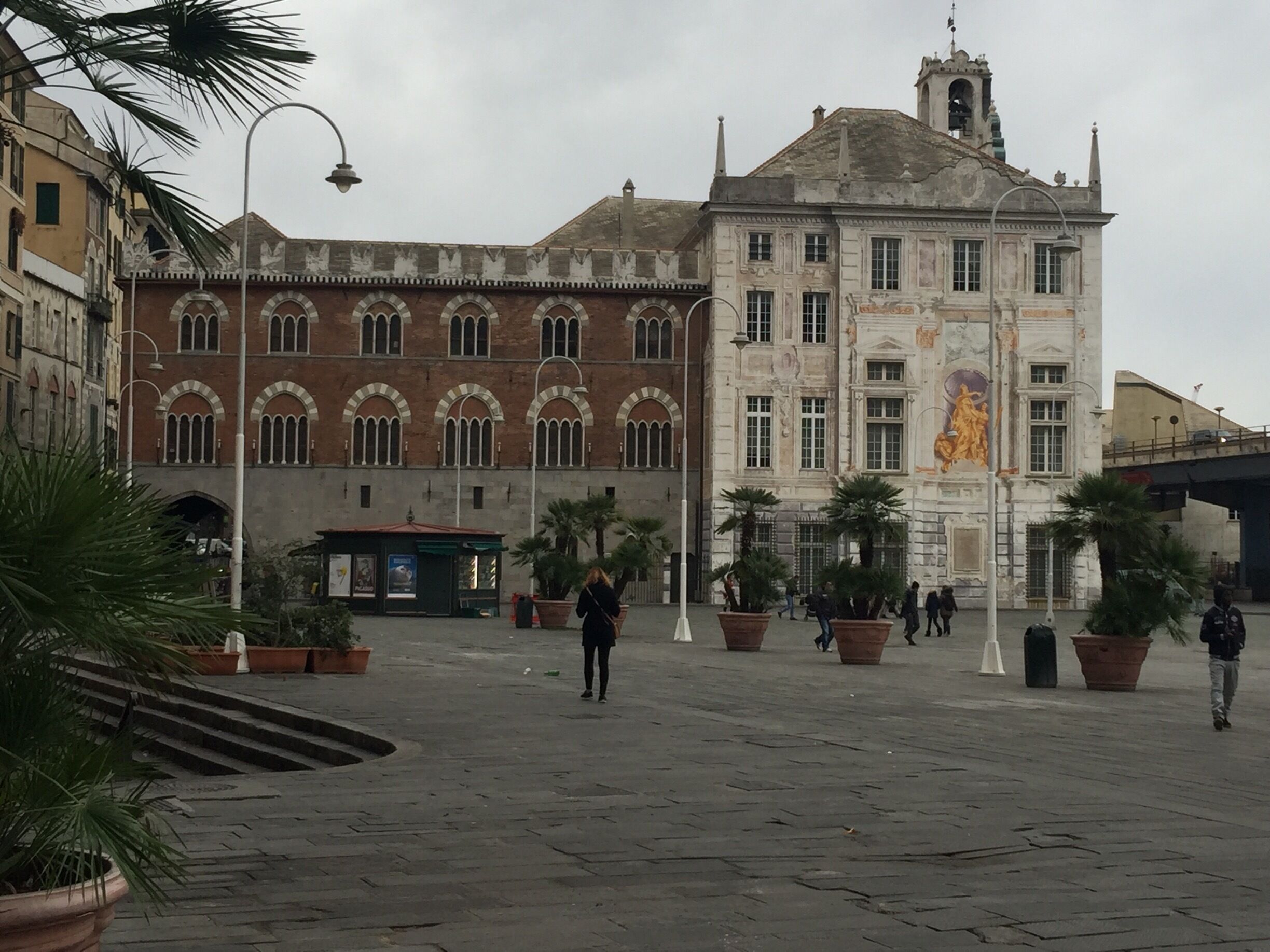 A historic square with a large building featuring arched windows and a statue.