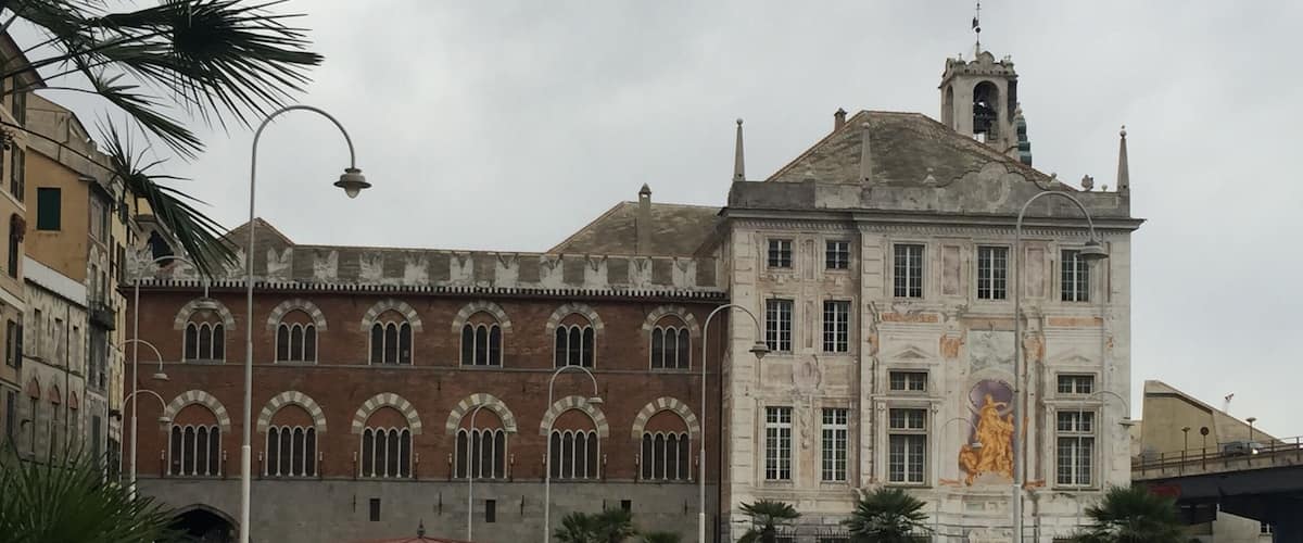 A historic square with a large building featuring arched windows and a statue.