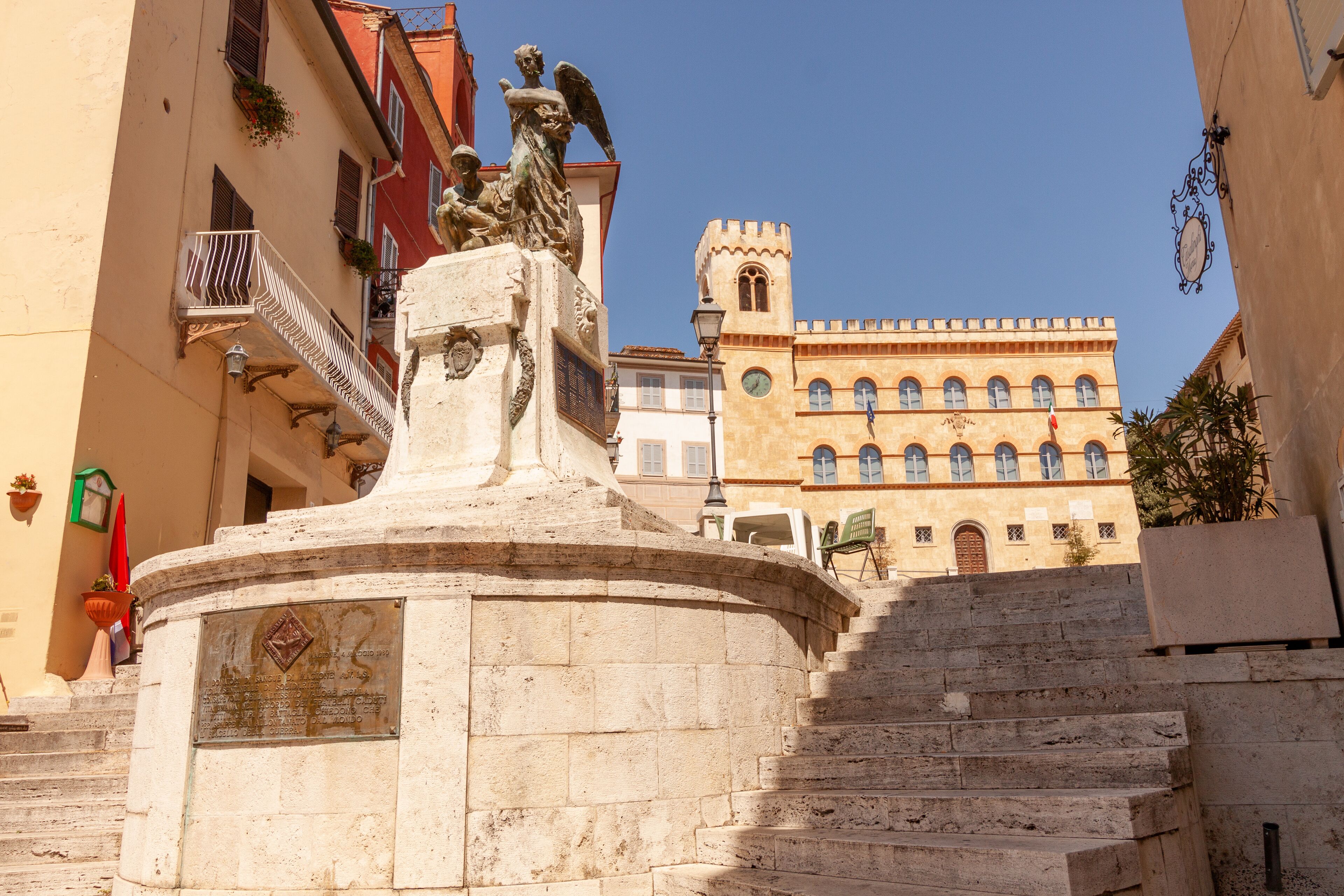 A stone monument with inscriptions, a staircase, and a building with arched windows in the background.