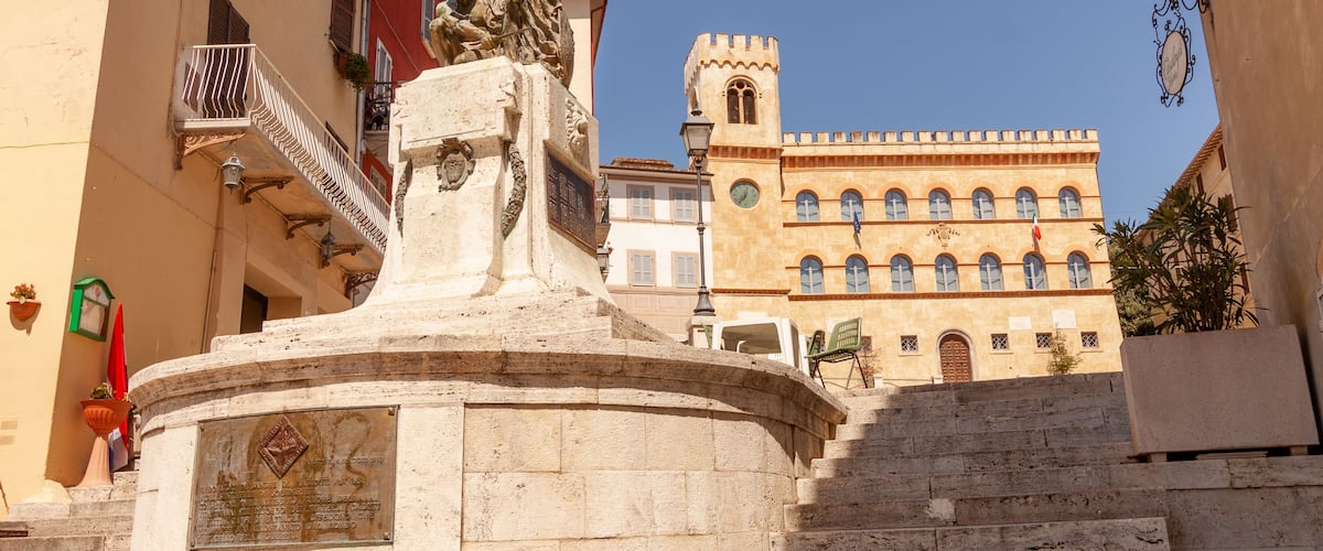 A stone monument with inscriptions, a staircase, and a building with arched windows in the background.