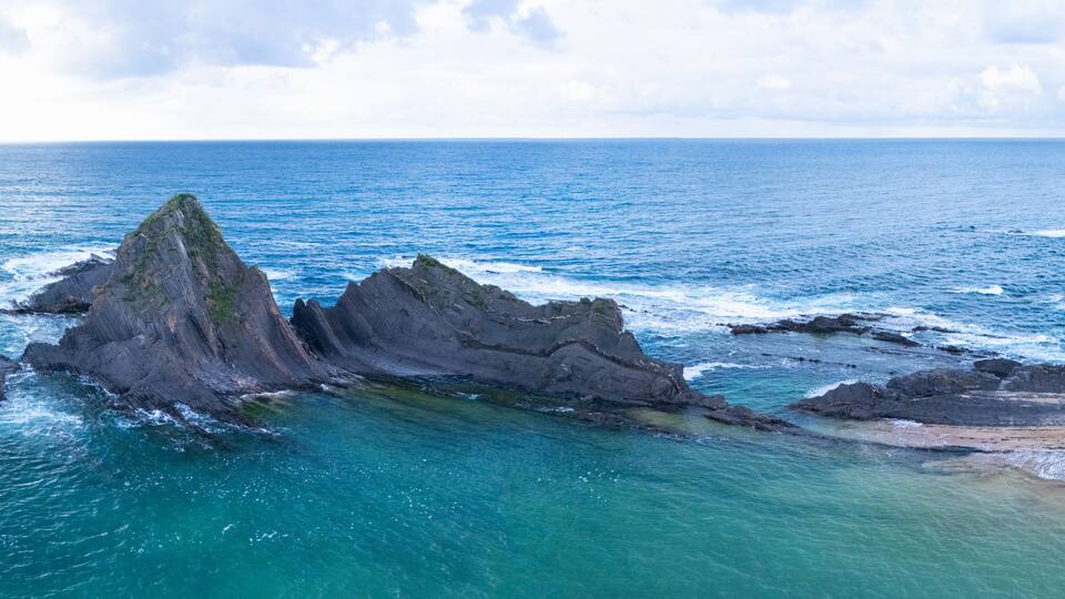 A coastal landscape with prominent rock formations and clear turquoise waters.