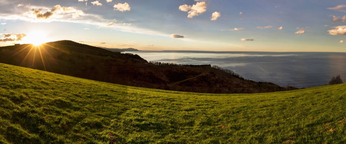 A grassy hillside with a view of the ocean and a distant mountain range.