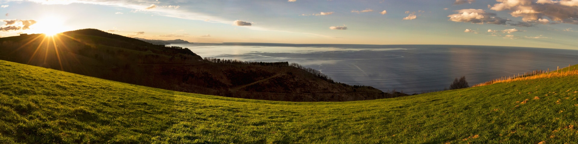 A grassy hillside with a view of the ocean and a distant mountain range.