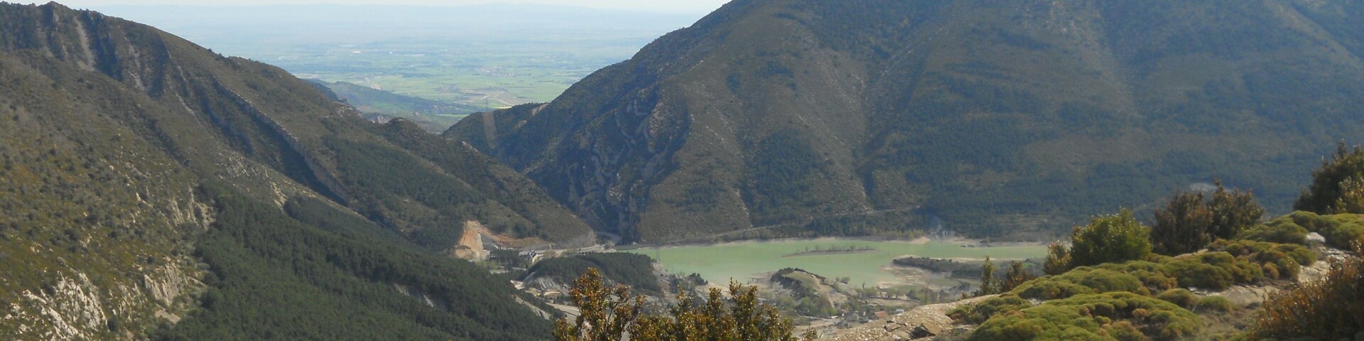 A mountainous landscape with a valley, dense forest, and a distant view of a lake.