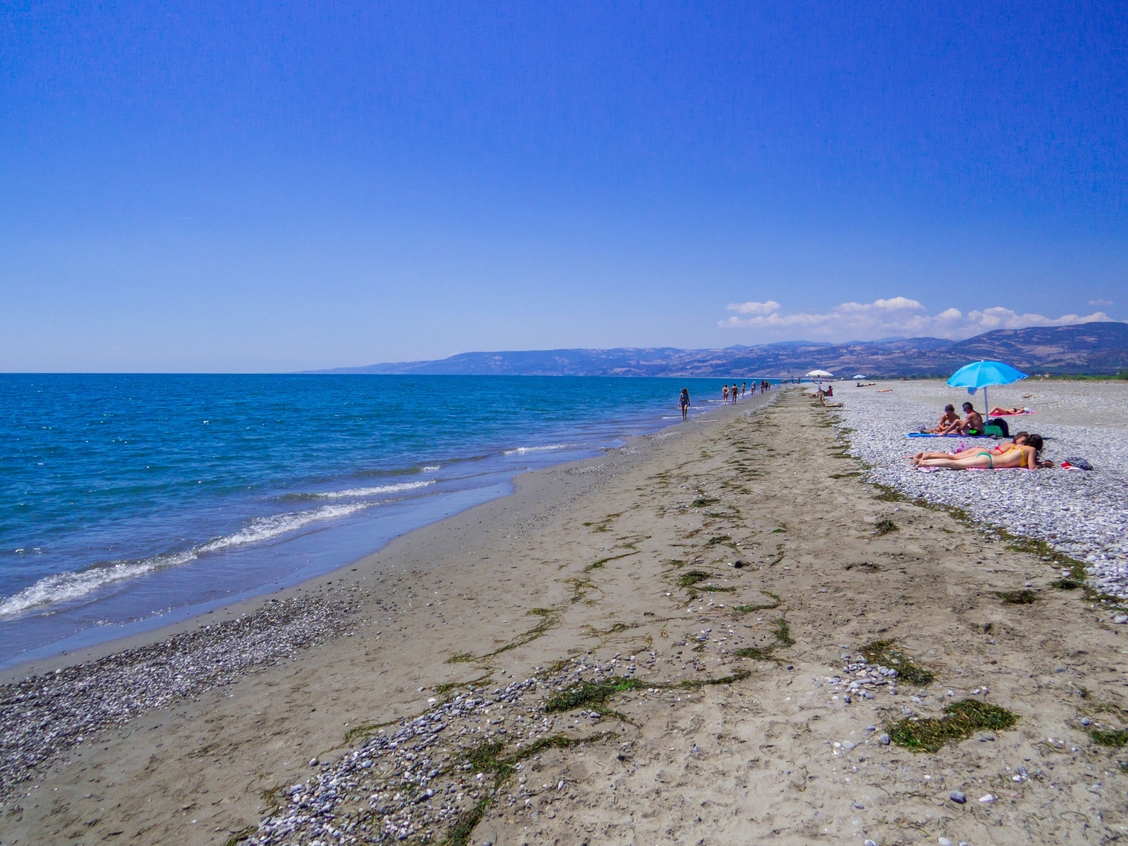 A pebbly beach with people sunbathing and walking along the shore.