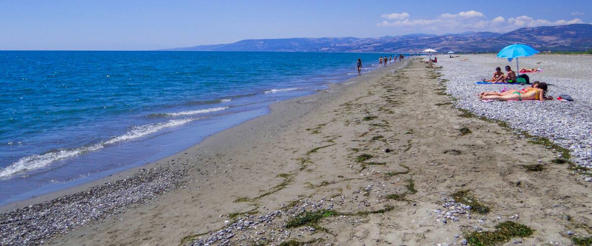 A pebbly beach with people sunbathing and walking along the shore.