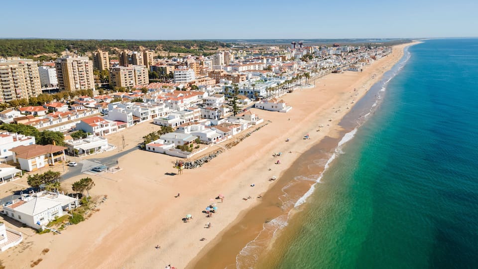 A coastal cityscape with a long sandy beach, dense residential buildings, and a clear blue sea.