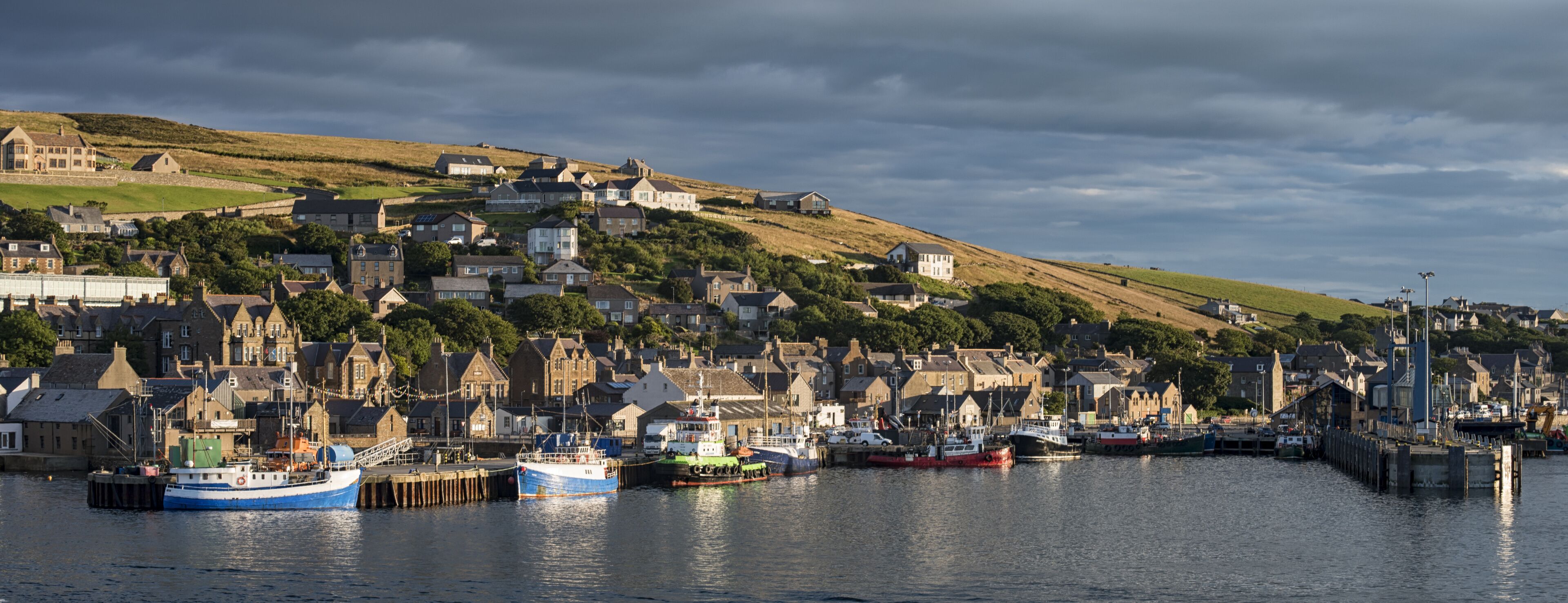A coastal town with a harbor, boats, and houses on a hillside.