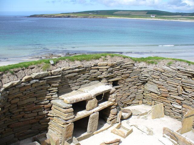 A stone structure by the sea with a view of the ocean and distant hills.