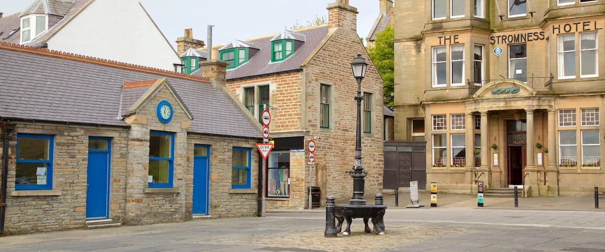 Een straat met keien, historische stenen gebouwen, een klokkentoren en een bord voor Hotel Stromness.