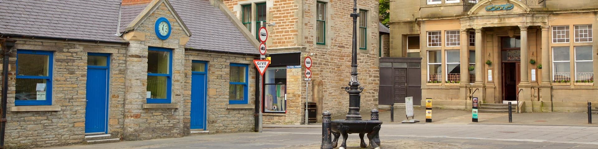 A cobblestone street with historic stone buildings, a clock tower, and a sign for The Stromness Hotel.