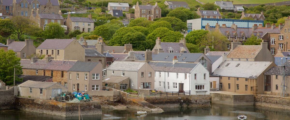 A coastal town with stone buildings, a harbor with boats, and a hill in the background.