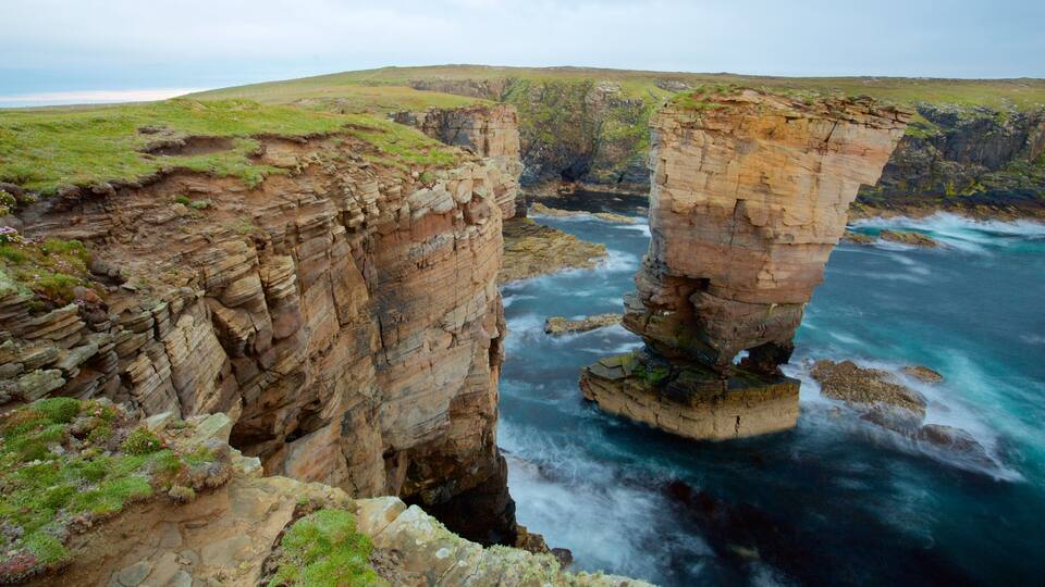 A coastal cliff formation with layered rock structures and a body of water below.