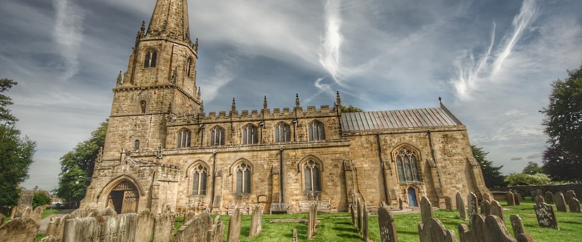 A historic church with a tall spire and a graveyard in front.