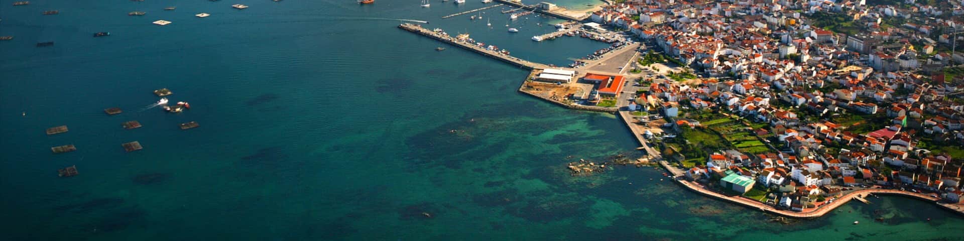 An aerial view of a coastal town with a marina, clear blue waters, and surrounding islands.