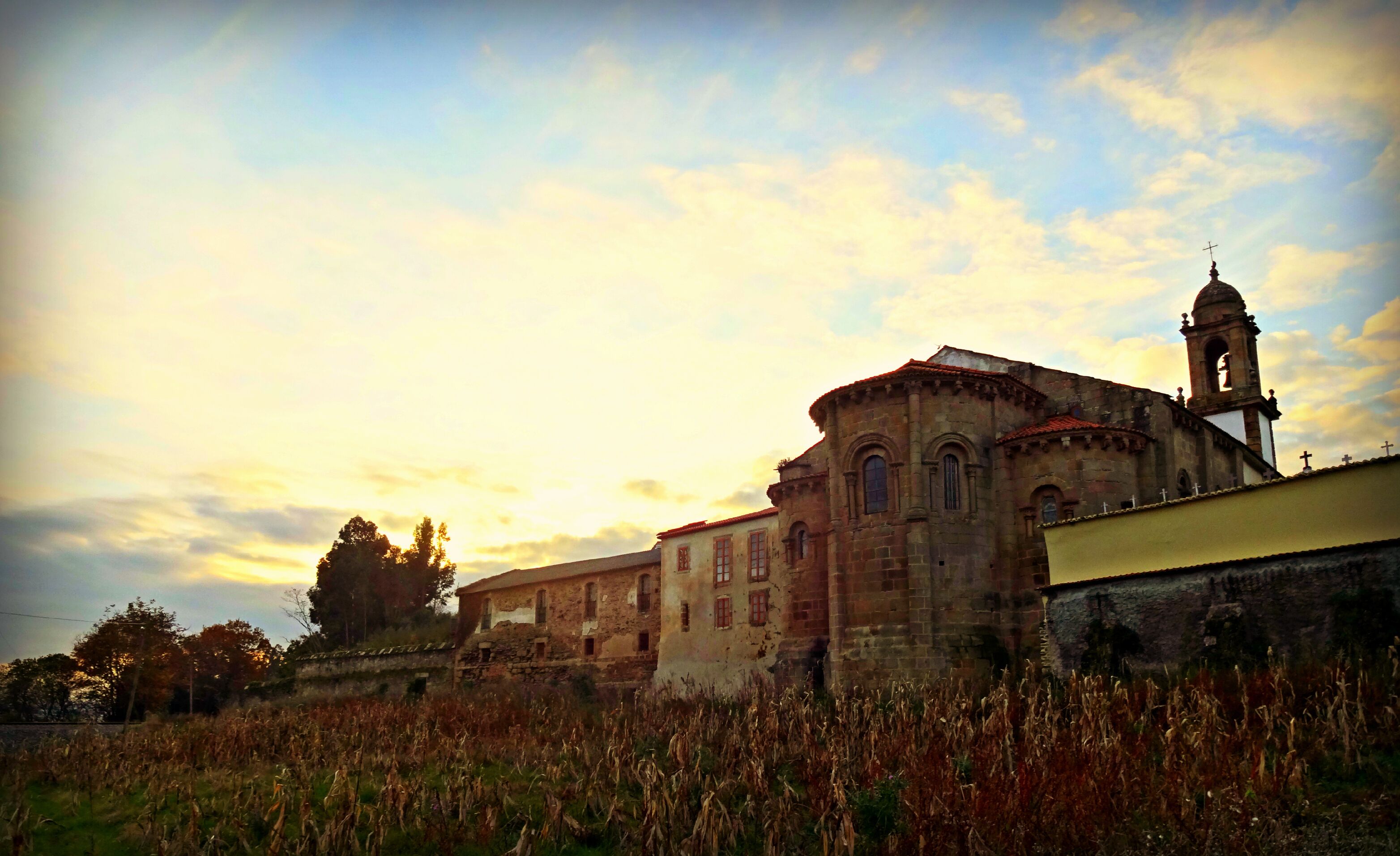 An old church with a bell tower and a field of dry grass in the foreground.