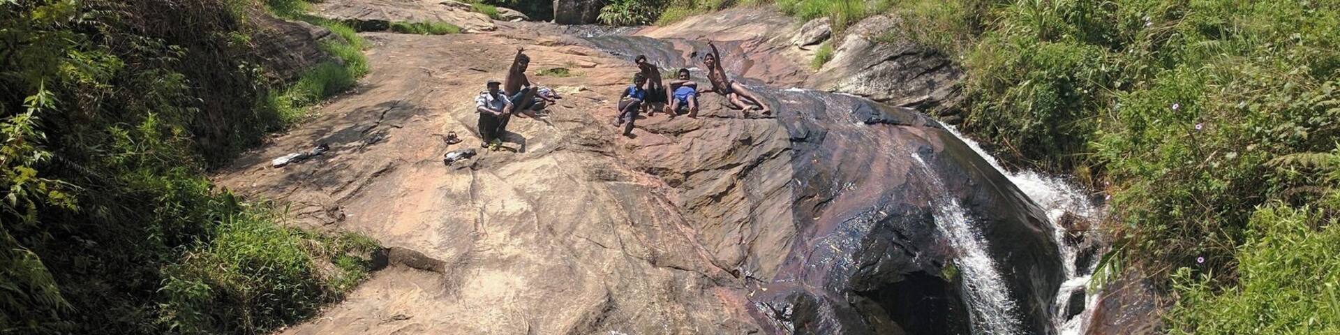 A rocky waterfall in a forested area with people observing the scene.
