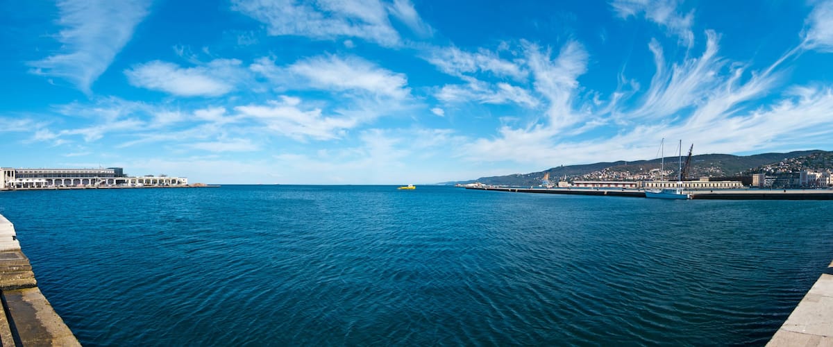 A coastal cityscape with a clear blue sky, calm sea, and a promenade.