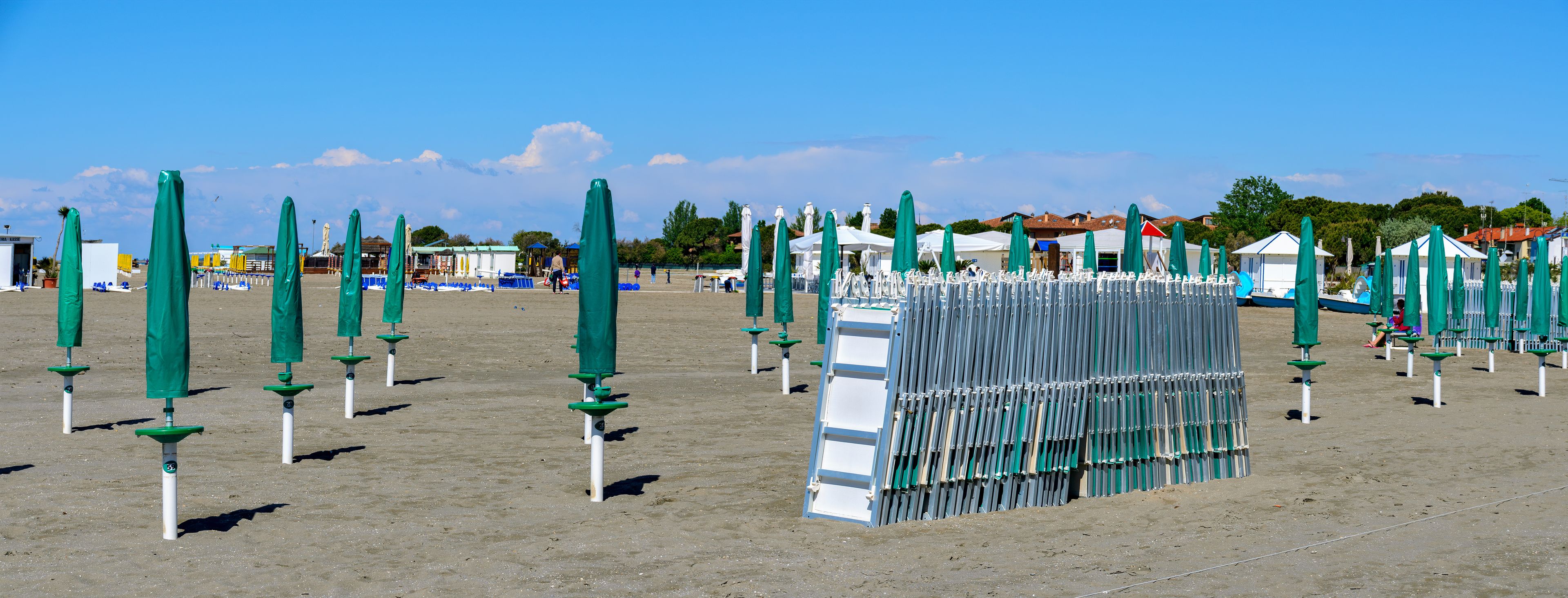 Une plage bordée de rangées de parasols verts et de chaises longues blanches.