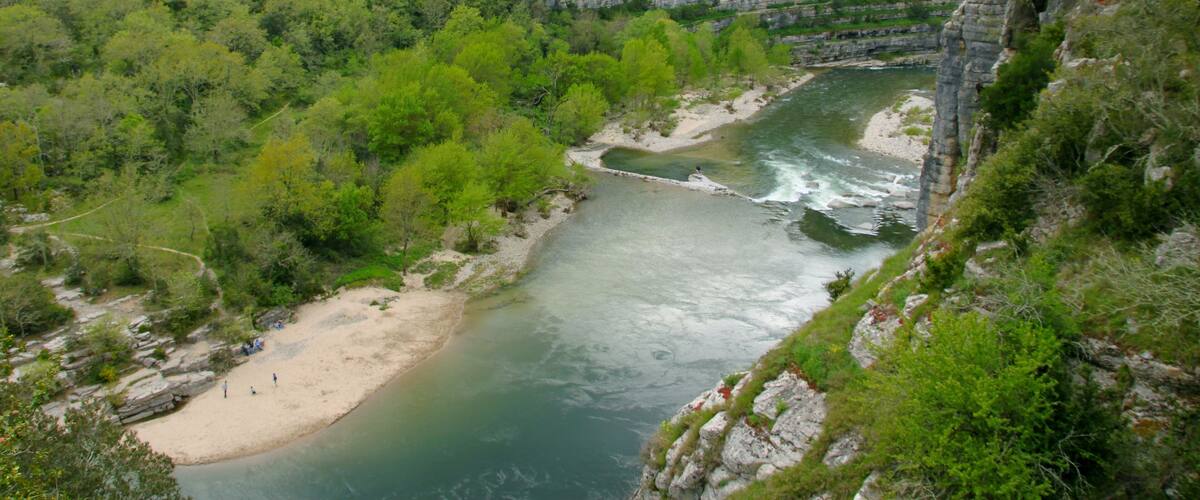 A river flowing through a canyon with a sandy beach and dense green vegetation.