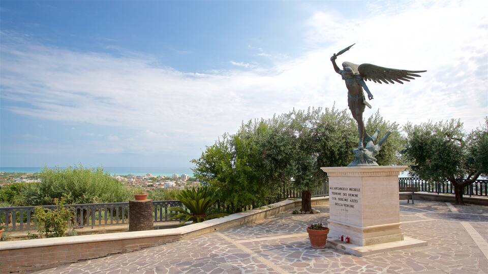 A statue of an angel with wings on a pedestal, overlooking a coastal town.
