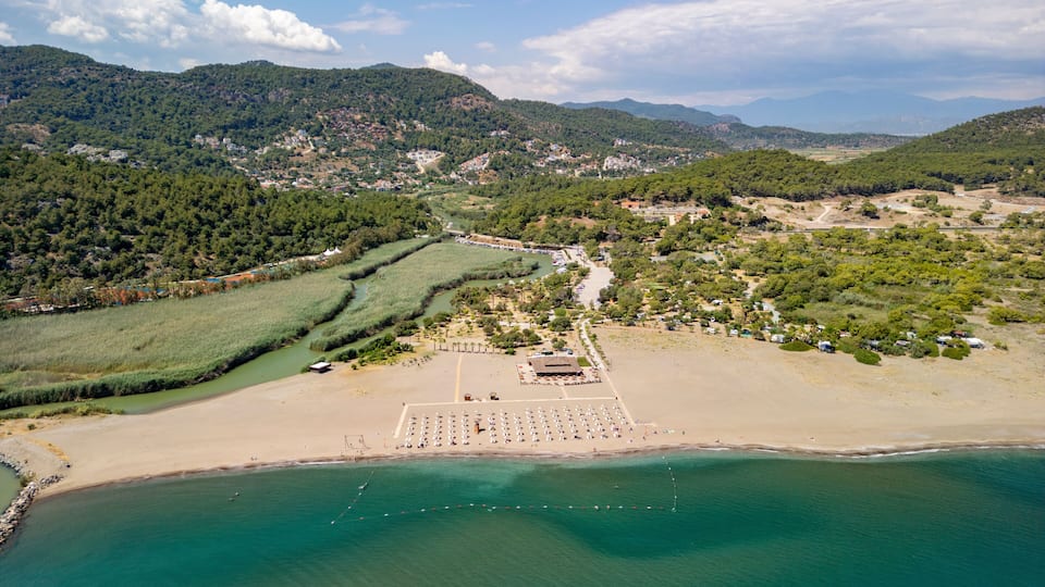 An aerial view of a coastal area with a sandy beach, a river, and a mountainous landscape in the background.