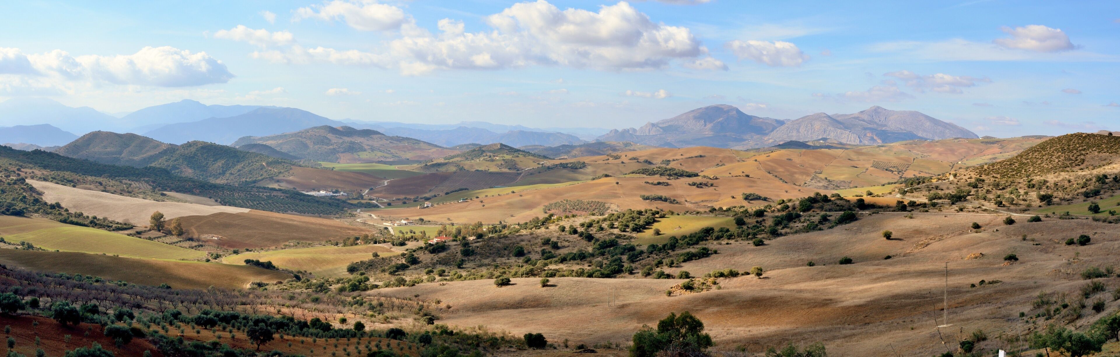 Rolling hills, a valley, and distant mountains under a partly cloudy sky.