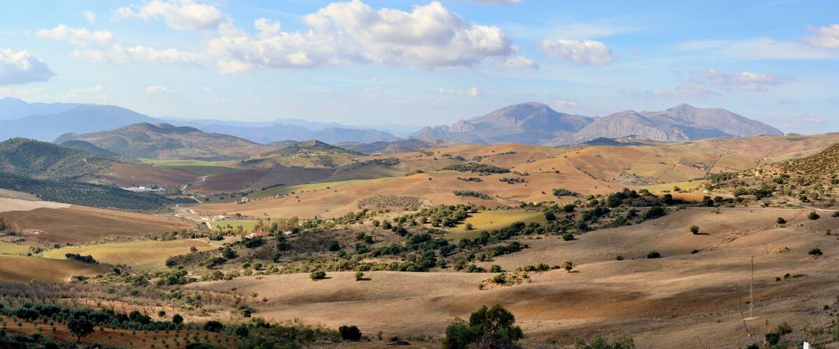 Rolling hills, a valley, and distant mountains under a partly cloudy sky.