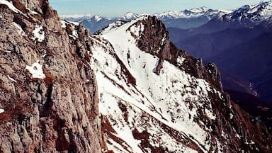 A rugged mountain landscape with snow-covered peaks and a clear blue sky.