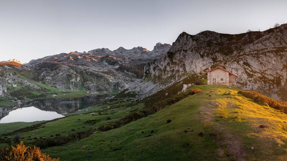 A mountain landscape with a lake, a small building, and a path leading up the hill.