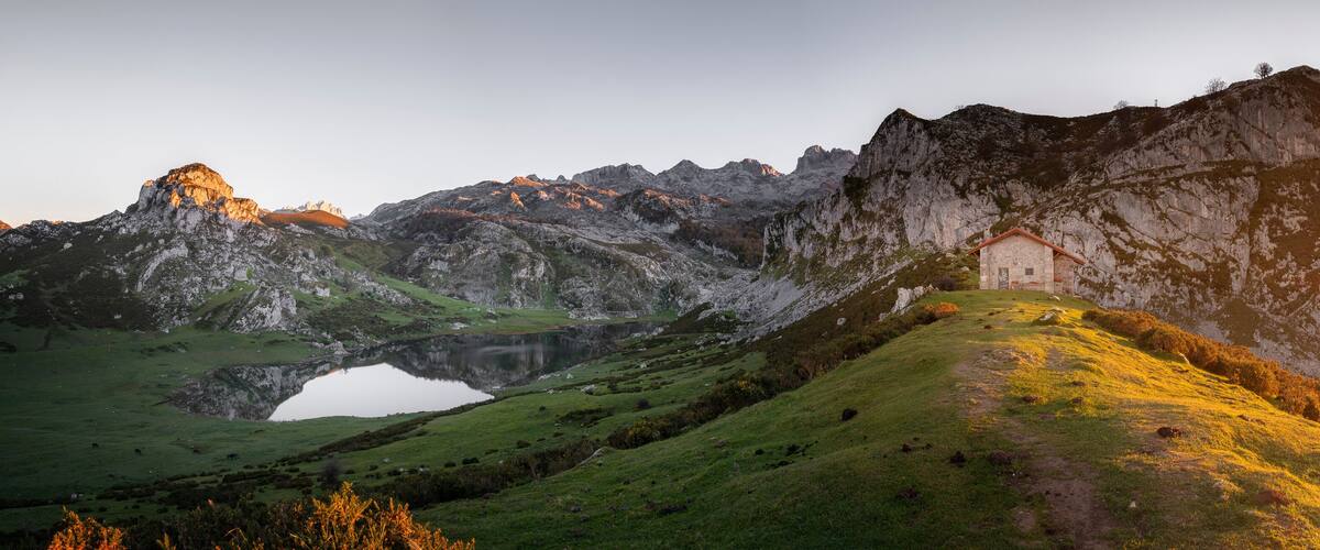 A mountain landscape with a lake, a small building, and a path leading up the hill.